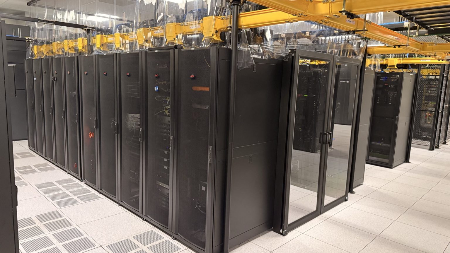 Row of cabinets with containment curtains under a yellow fiber raceway on a raised datacenter floor